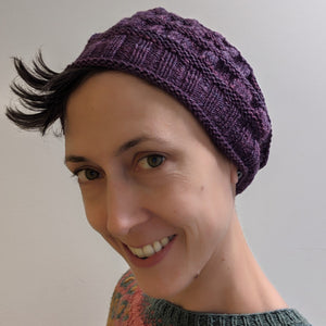 Person smiling wearing a purple hand knitted hat