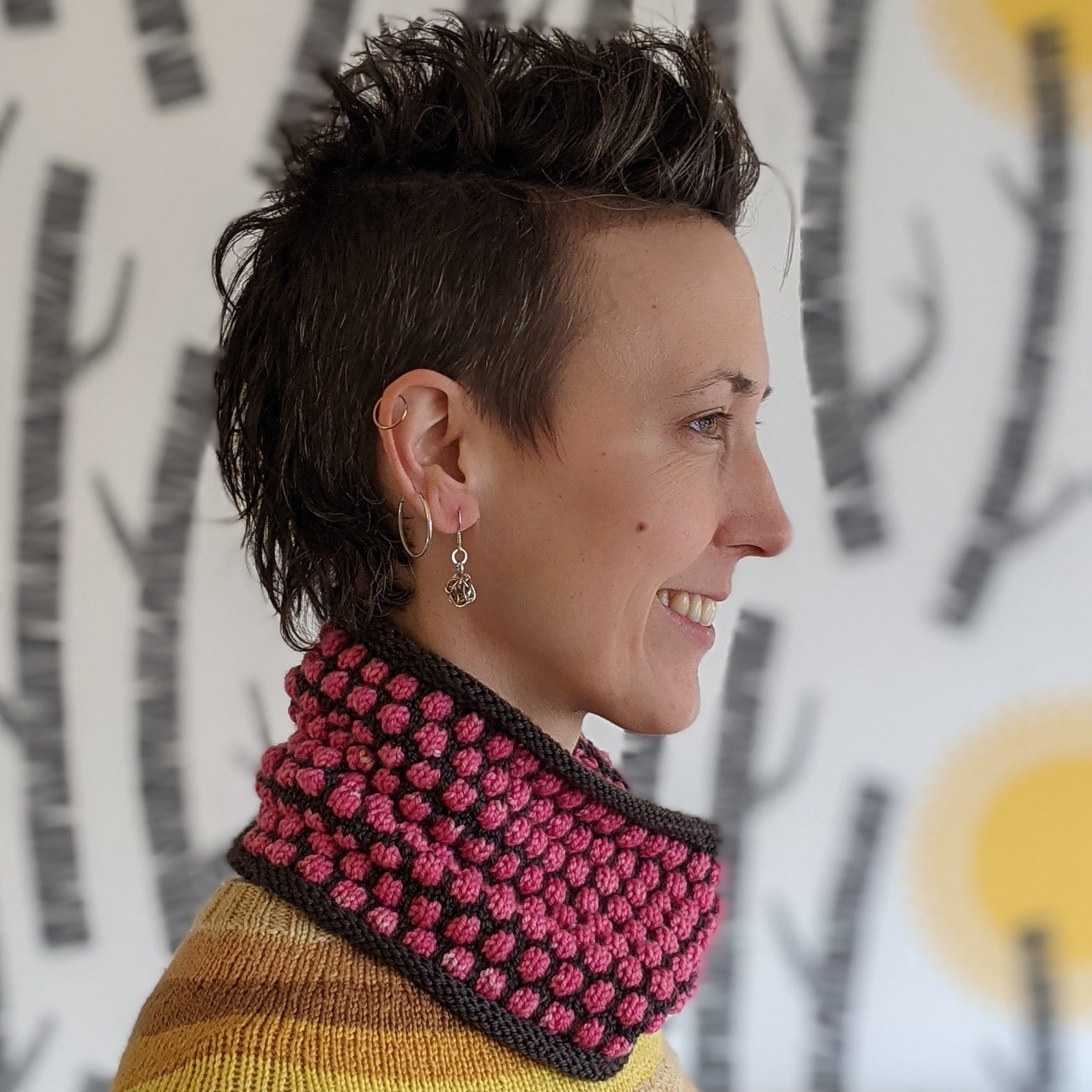 Side view of person smiling wearing a pink and grey hand knitted cowl